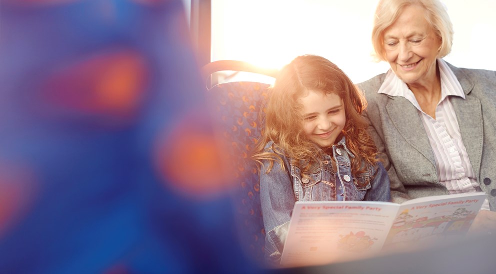 A child and her Grandma reading a book on the bus