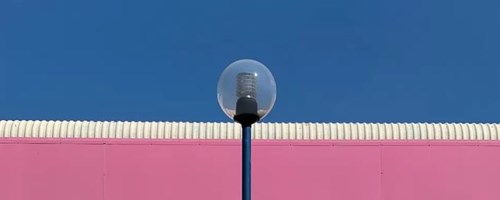 Tom Hicks image of lampost against white metal building with pink strip and blue sky
