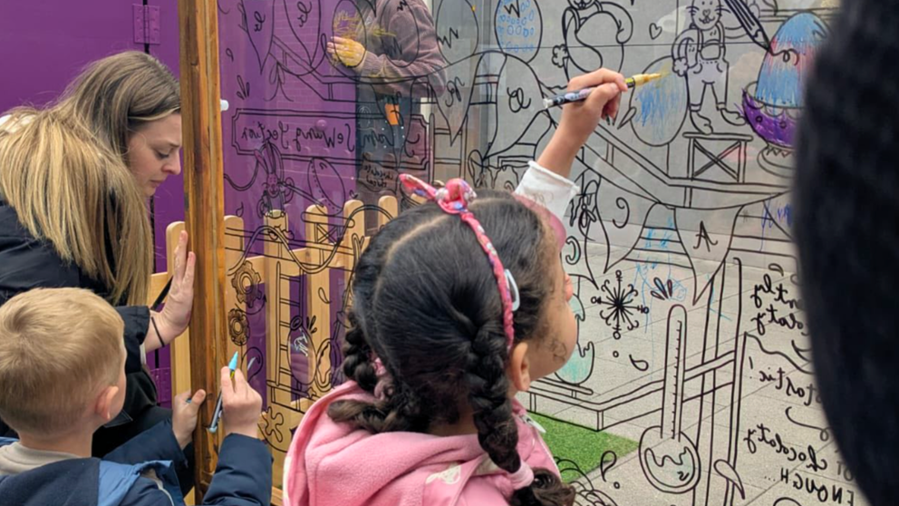 An image of children drawing on a glass screen outside New Square shopping centre