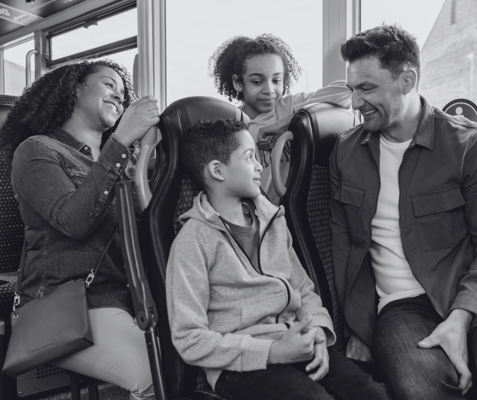 A family of four sat on the bus together and smiling.