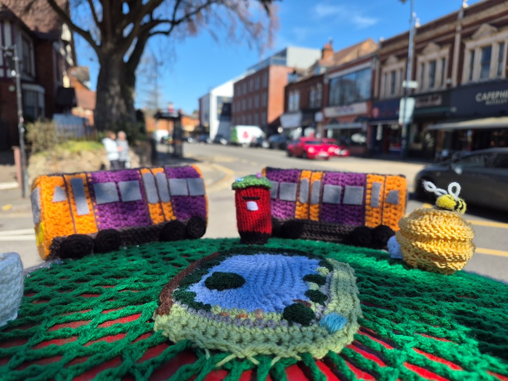 A close up image of a knitted postbox topper. The focus is on a knitted West Midlands Railway train.