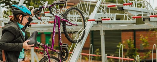 woman in cycle helmet putting push bike into station cycle parking